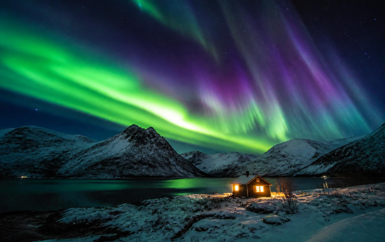 Northern Lights Planning Support — Northern lights over snow-covered arctic mountains and a lit cabin